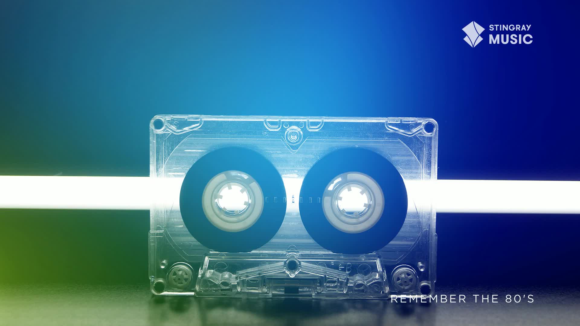 A transparent cassette tape sits centered, its spools a deep blue. A bright, horizontal line of light cuts through the tape's body, a nostalgic nod to Stingray Everything '80s in Canada.

