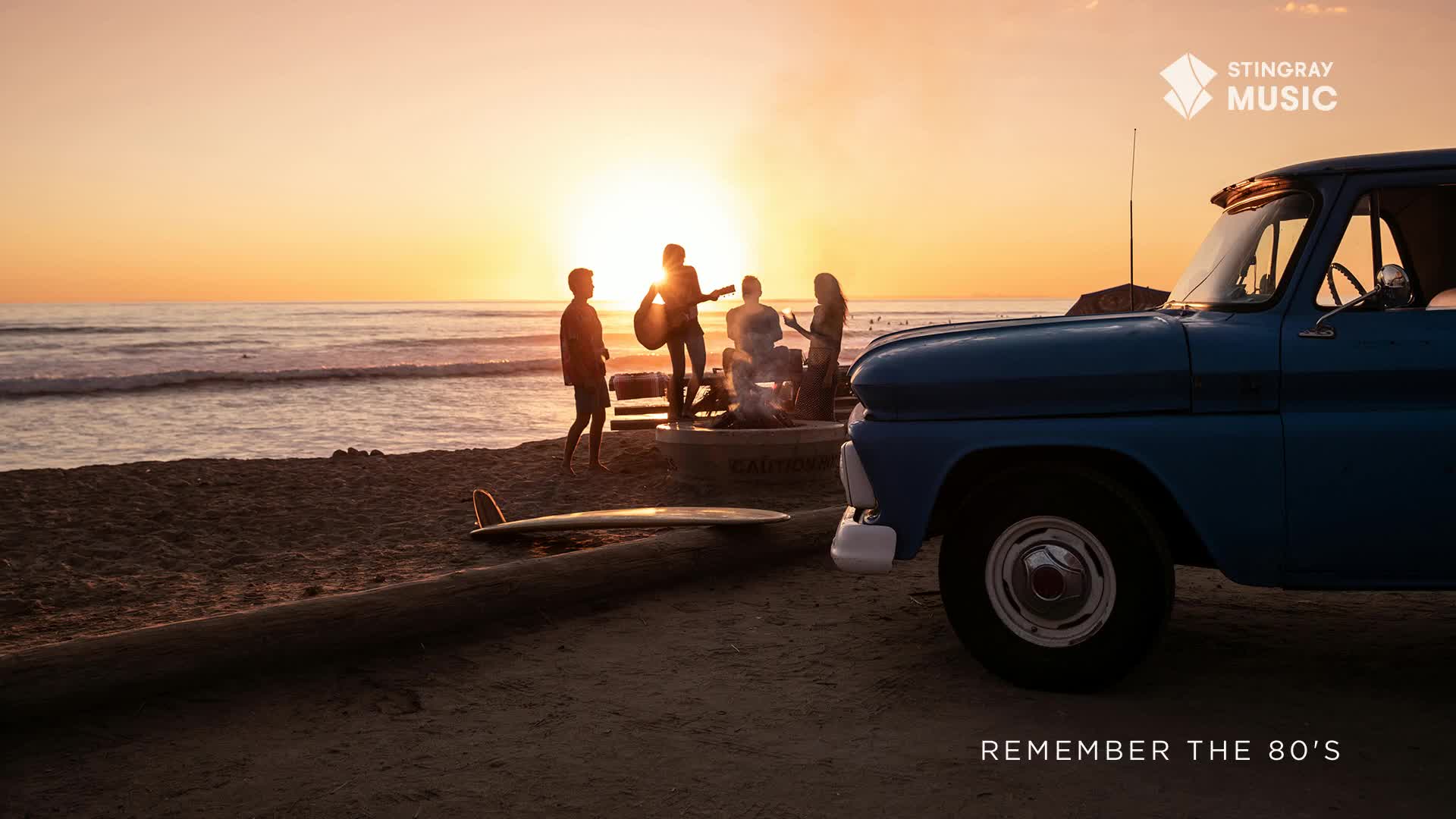 The sun dips low, casting long shadows as a group gathers around a fire pit. A vintage blue truck sits parked on the beach, the perfect backdrop for a Canadian summer evening and a Stingray Everything '80s vibe.
