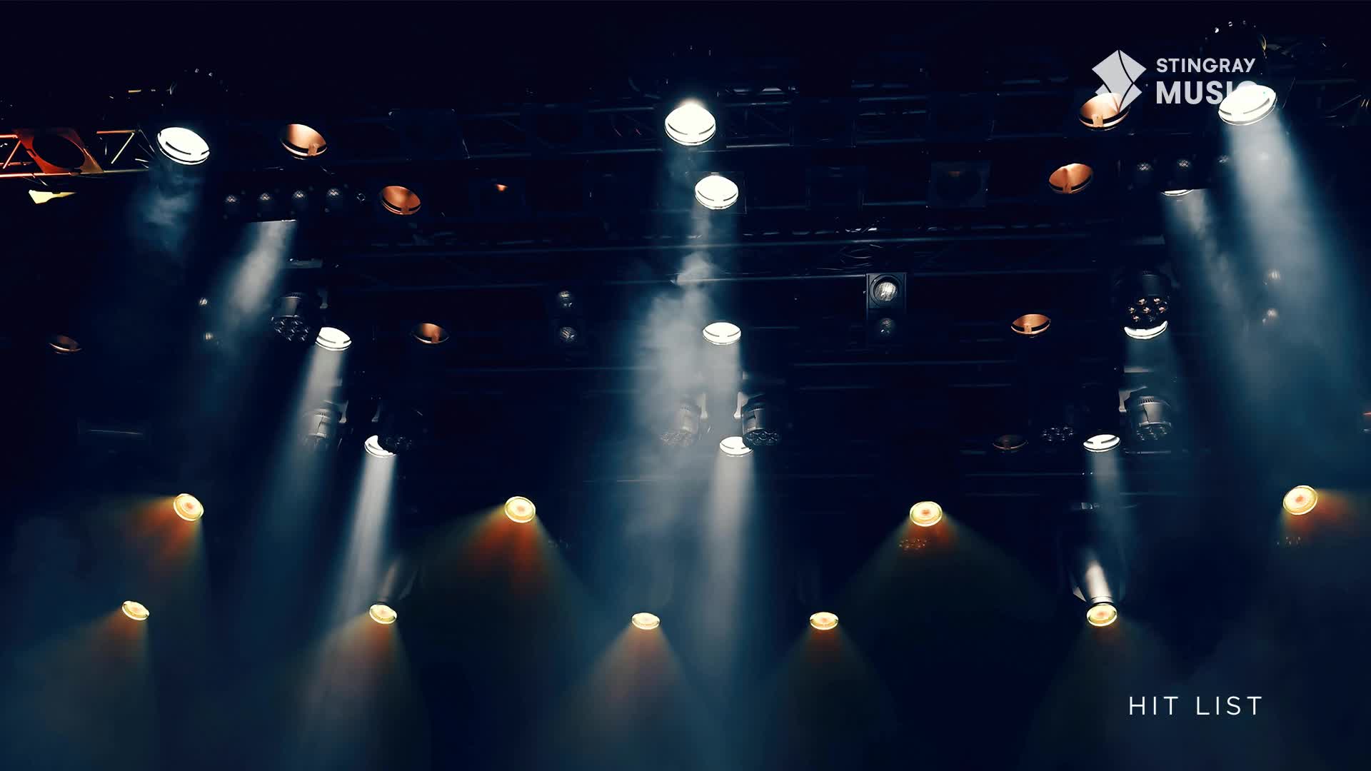 Bright spotlights pierce the darkness, illuminating a hazy atmosphere above the stage. The Stingray Hit List logo is visible, hinting at a music performance in Canada.
