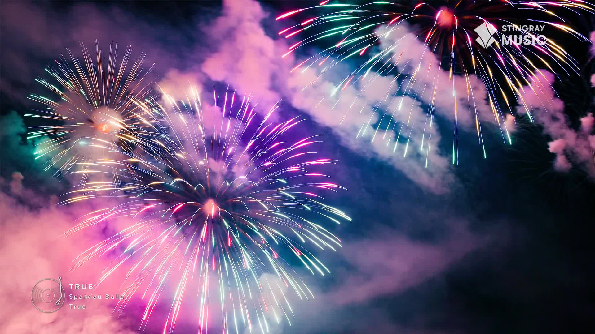 Bright bursts of pink, purple, and green light explode against the dark sky. Wisps of smoke drift through the air, remnants of the dazzling display, perhaps a holiday celebration in Canada, brought to you by Stingray Holiday Hits.
