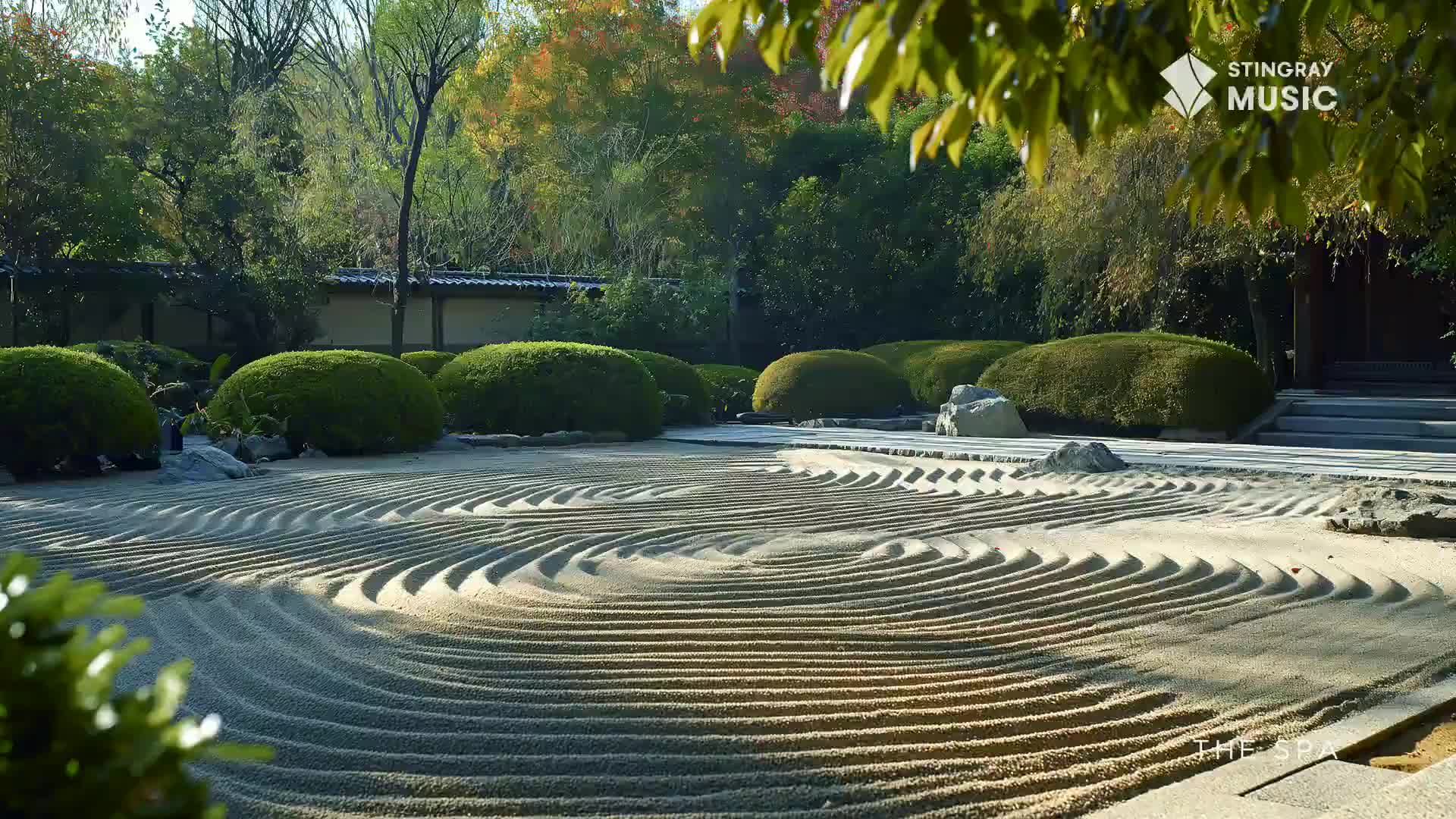 The raked sand in this Japanese garden creates a serene pattern, a quiet space at The Spa. Lush, sculpted bushes and trees surround the tranquil scene.