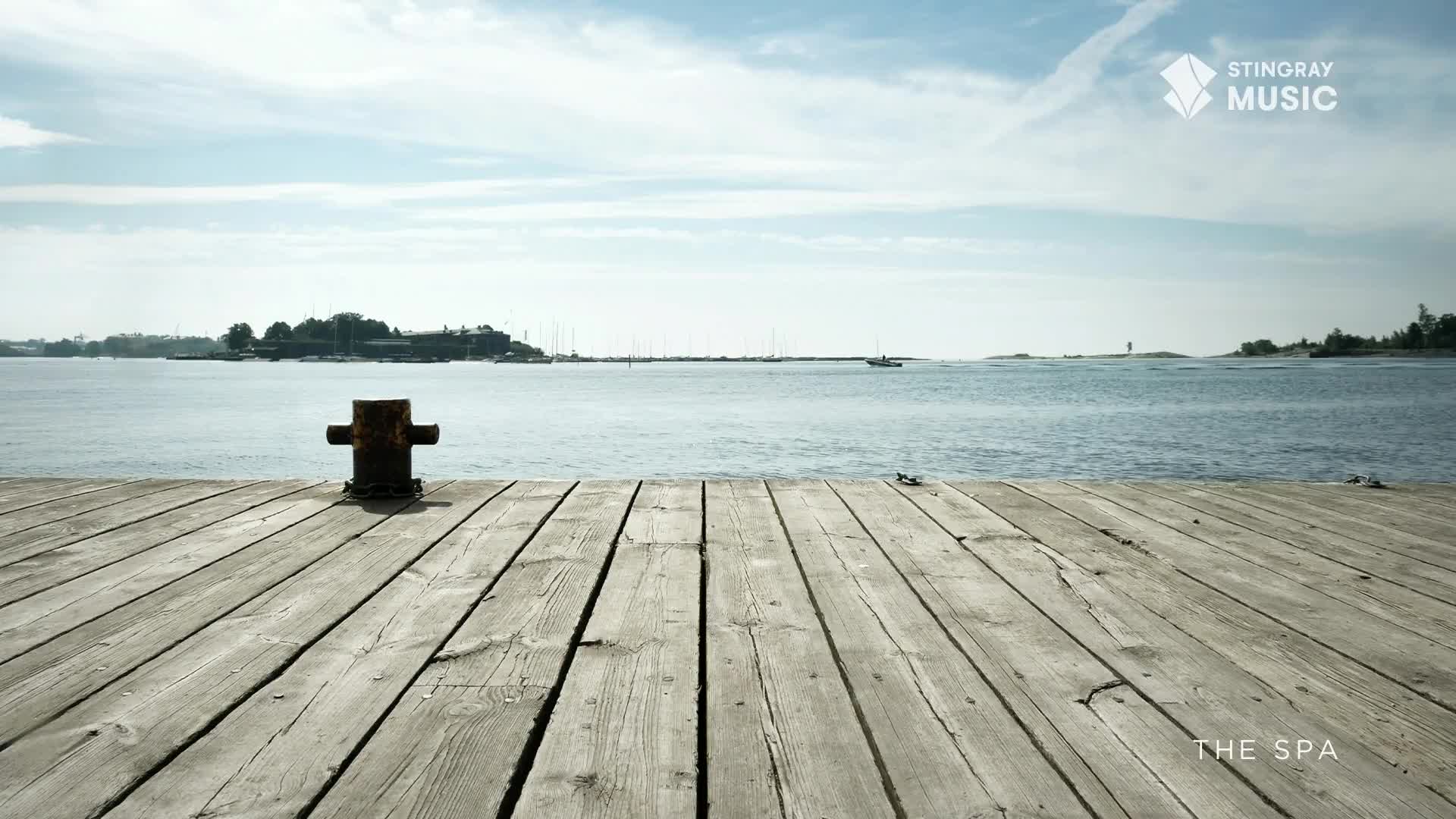 A small boat cuts through the calm water, heading towards a distant island. The weathered planks of the dock stretch out before me, leading to the tranquil expanse of the Canadian bay.
