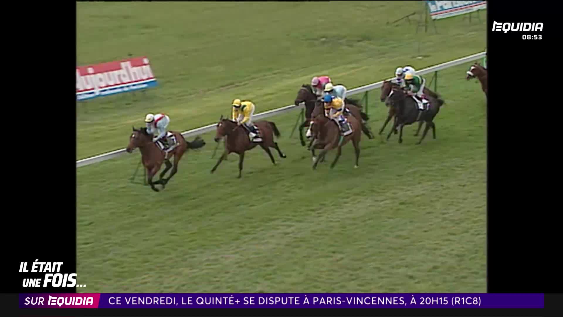 The horses are running hard, their jockeys leaning forward. A brown horse with a white-capped jockey pulls ahead on the left.