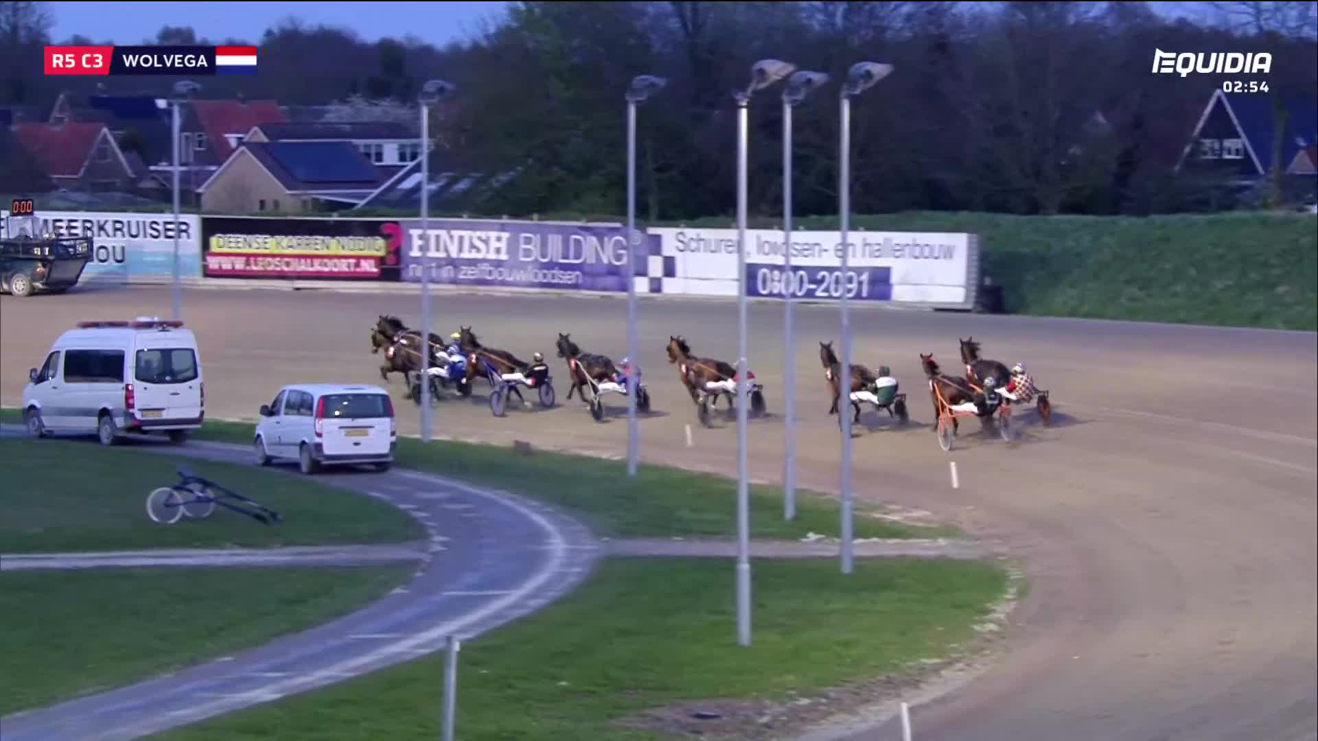 The horses are thundering around the bend, their hooves kicking up dust. A few sulkies are bunched together, jostling for position on the track.