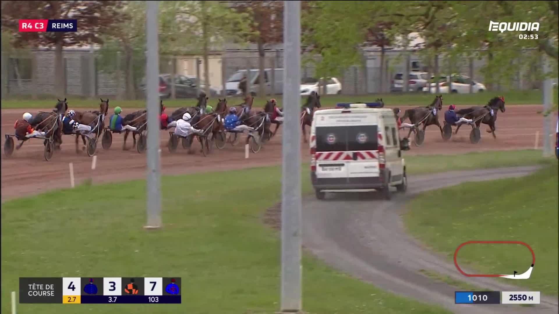The horses are thundering down the dirt track in Reims. A white van with red and white stripes follows closely behind the pack.
