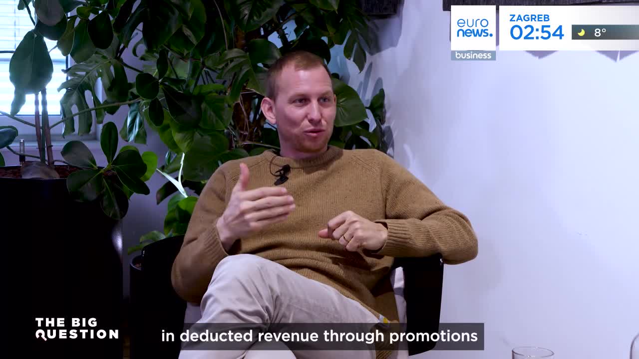 A man in a tan sweater gestures with his hands, speaking into a microphone. The Euronews logo and a clock showing 02:54 in Zagreb are visible in the upper right corner.