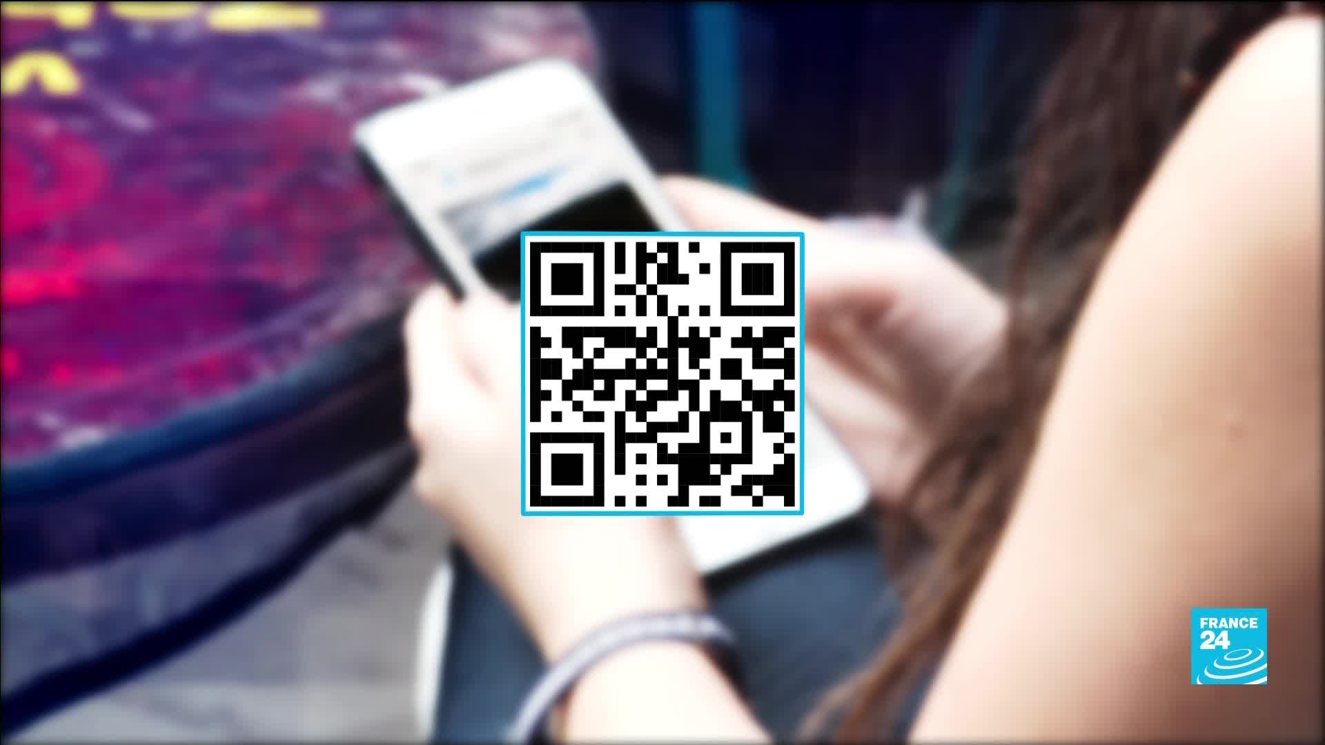 A woman's hands hold a smartphone, its screen displaying a QR code. The France 24 logo is visible in the corner.