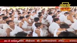 A large group of people in white clothing are seated, facing forward. The scene is from Aastha Bhajan, a religious program in India.
