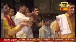 Men in brightly colored clothing stand close together, some with their hands raised. The Aastha Bhajan logo is visible above them, suggesting a religious broadcast from India.
