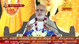 A man with a white beard and glasses speaks into two microphones, gesturing with his hands. He's seated in front of a backdrop with a floral arrangement and text in Hindi.
A man with a white beard and glasses speaks into two microphones, gesturing with his hands. He's seated in front of a backdrop with a floral arrangement and text in Hindi.