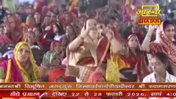 A crowd of people, mostly women in colorful saris, are gathered, many with their hands raised in prayer or devotion. The Aastha Bhajan logo is visible, indicating a religious broadcast from India.