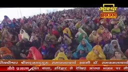 A vast crowd of people, many wearing colorful shawls, are gathered together. They are all facing in the same direction, listening intently.