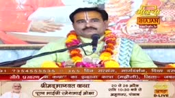A man with a tilak on his forehead speaks into a microphone, draped in colorful garlands. He is broadcasting a devotional program, likely a Bhajan, from India.