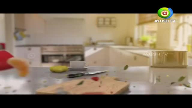 A bright orange slice floats in the air, landing on a kitchen counter. A knife rests beside a cutting board, with a few scattered leaves and a strawberry.