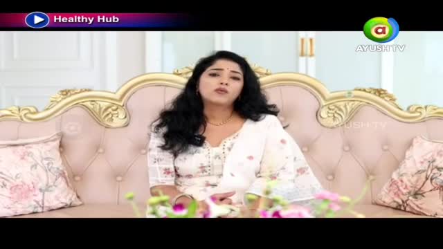 A woman in a white salwar kameez speaks from a plush pink sofa, a gold-trimmed frame behind her. The Ayush TV logo appears in the corner, signaling a program from India.