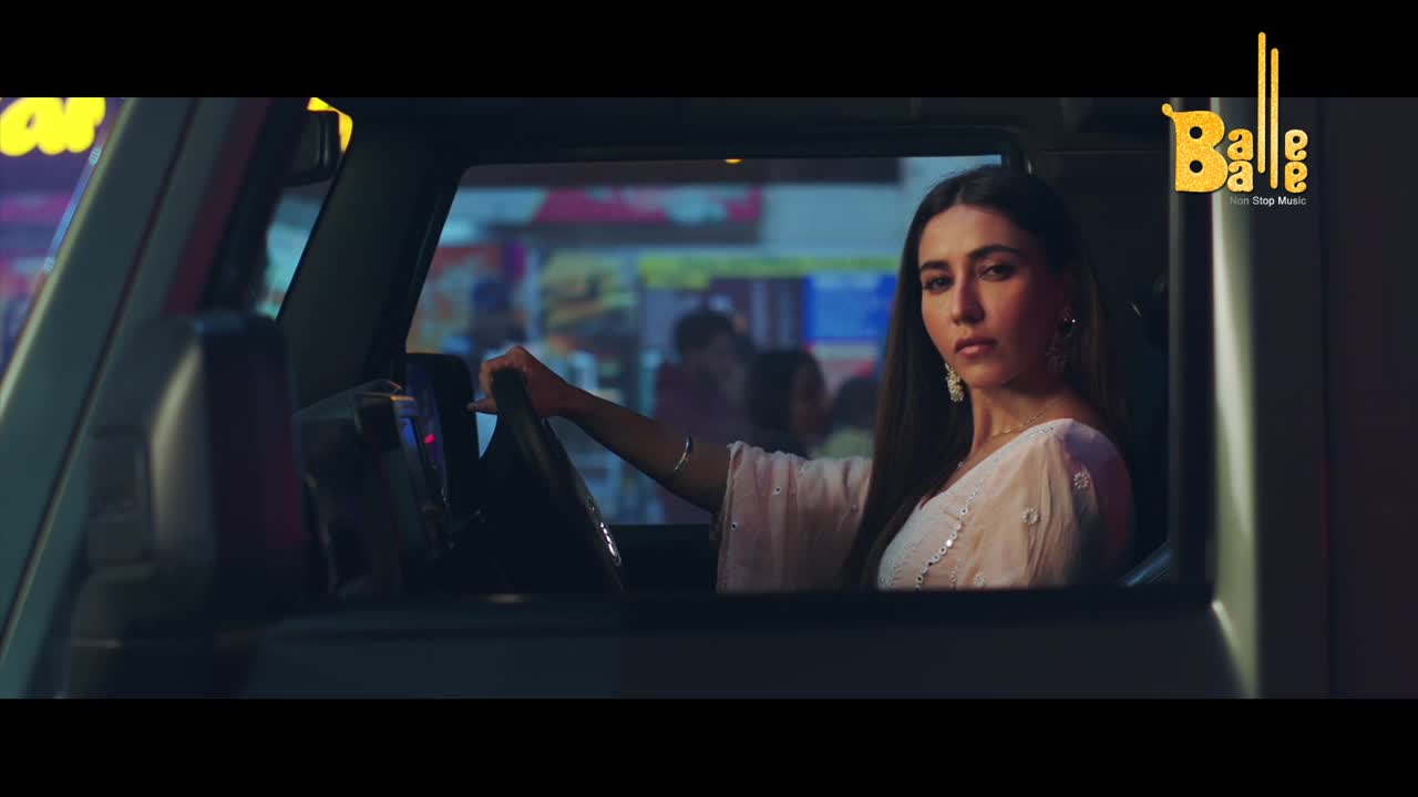 A woman in a white outfit grips the steering wheel of a car, her gaze fixed ahead. The glow of neon signs reflects on the car's interior as the Balle Balle logo appears.