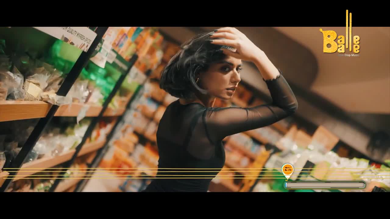 A woman in a sheer black top runs her fingers through her short, dark hair. Shelves stocked with goods stretch behind her, a familiar sight in any Indian market.