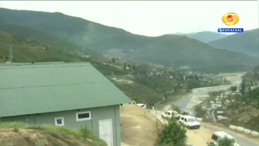 A line of white vehicles navigates a winding road through a valley in Arunachal Pradesh. The DD Arun Prabha logo marks this view of the Indian landscape.