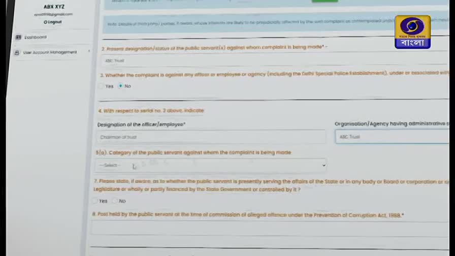 A form is displayed on a screen, showing fields for reporting complaints against public servants. The DD Bangla logo is visible in the top right corner.