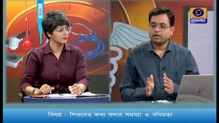 A man in a blue shirt speaks animatedly, gesturing with his hands. Across from him, a woman in a maroon shirt listens intently. The DD Bangla logo is visible in the background.