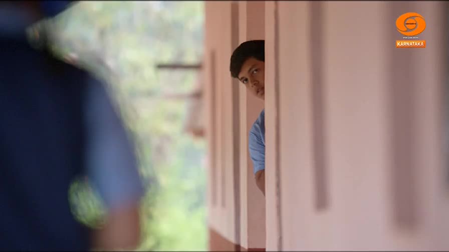 A young boy peeks around a pillar, his eyes wide. The faint DD Chandana logo suggests this is from a broadcast in Karnataka.