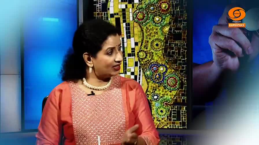 A woman in a coral-colored kurta speaks, her pearl necklace catching the light. Behind her, a vibrant mosaic artwork bursts with color, and a hand holds up a pair of glasses, framed by the DD Chandana logo.