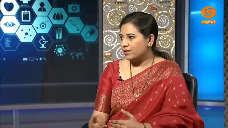 A woman in a red silk sari speaks animatedly, her hands gesturing. Behind her, a screen displays a grid of medical icons, with the DD Chandana logo visible on the right.