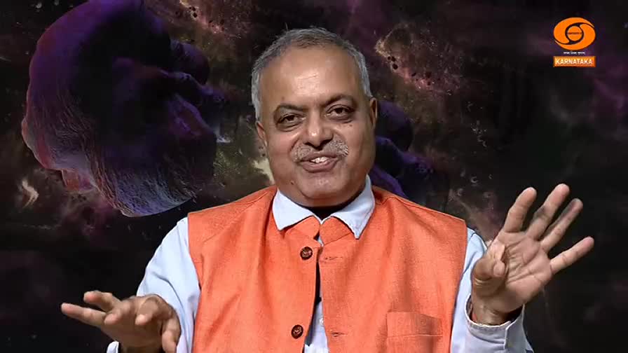 A man in an orange vest gestures with his hands, speaking animatedly. Behind him, a purple, abstract shape floats against a dark, cosmic background.