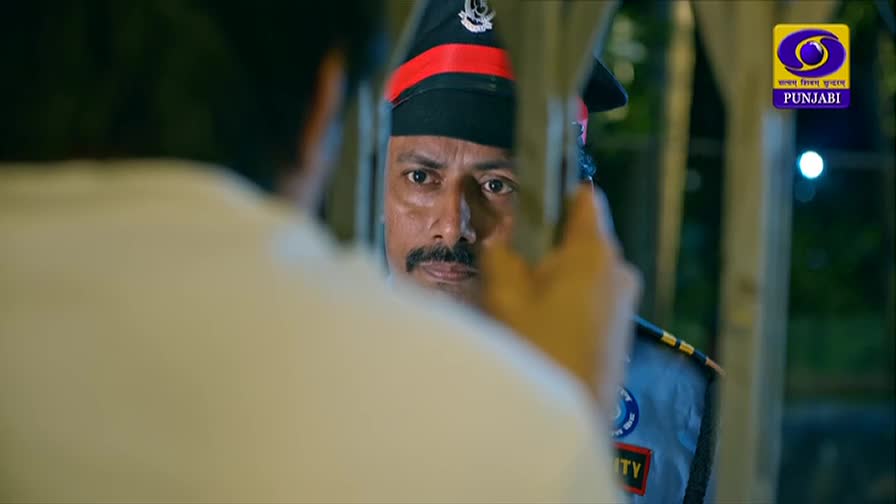 A man in a dark uniform with a red stripe on his cap stares intently. His face is framed by a blurred foreground, suggesting a close-up view through a barrier.