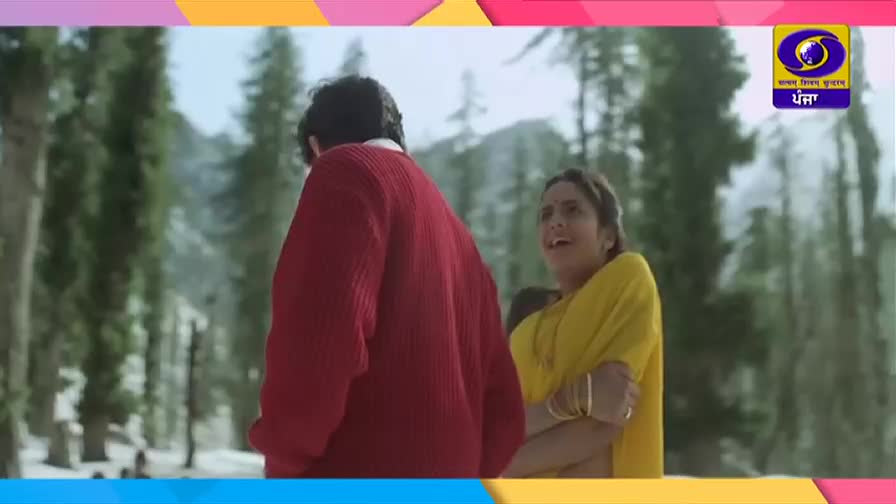 A man in a red sweater turns away as a woman in a bright yellow shawl looks on with a worried expression. The DD Punjabi logo is visible in the corner, suggesting this is a scene from an Indian production.