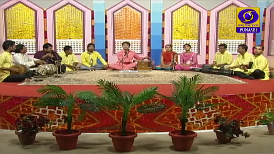 A group of musicians sits on a stage, some playing instruments while others sing. The DD Punjabi logo is visible in the corner of the screen. A group of musicians sits on a stage, some playing instruments while others sing. The DD Punjabi logo is visible in the corner of the screen.