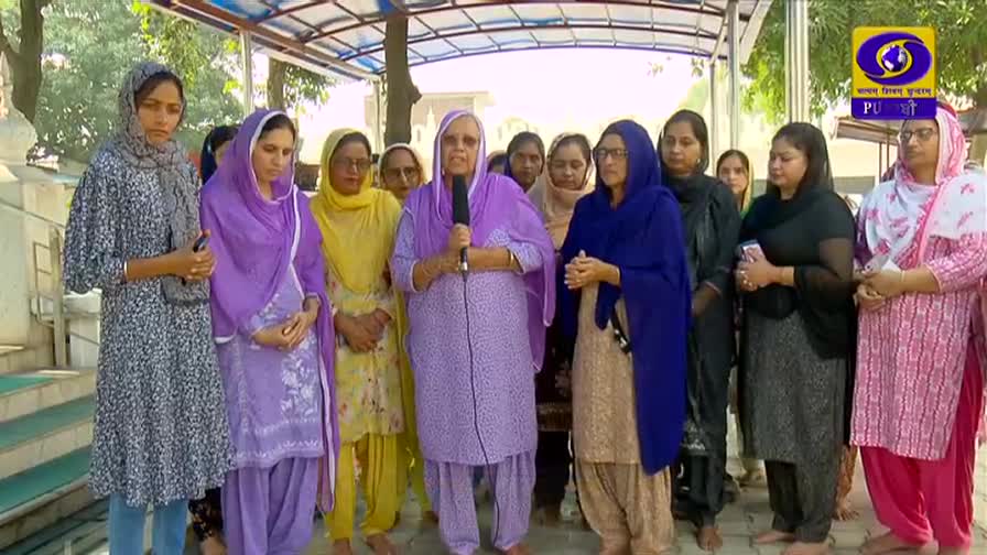 A woman in a lavender salwar kameez speaks into a microphone, surrounded by a group of women. The DD Punjabi logo is visible in the upper right corner. A woman in a lavender salwar kameez speaks into a microphone, surrounded by a group of women. The DD Punjabi logo is visible in the upper right corner.