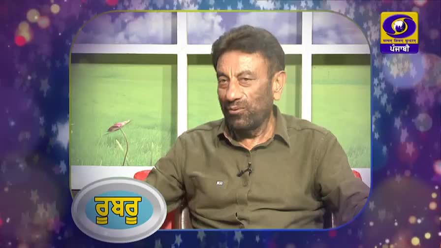 A man in a green shirt is speaking, his face animated. A graphic with Punjabi text hovers in the lower left corner of the screen. A man in a green shirt is speaking, his face animated. A graphic with Punjabi text hovers in the lower left corner of the screen.