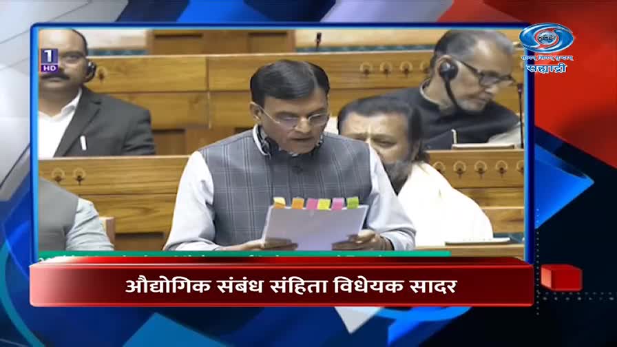 A man in a checkered vest reads from a document, its pages tabbed with colorful sticky notes. Behind him, other men in formal attire listen intently in a wood-paneled room.