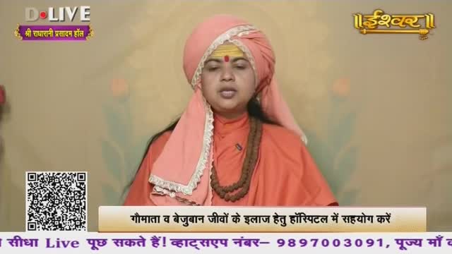 A person in saffron robes and a pink turban speaks, their face illuminated. A string of brown beads hangs around their neck.