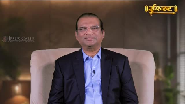 A man in a suit sits in a chair, speaking directly to the camera. The "Ishwar" logo appears in the upper right corner.