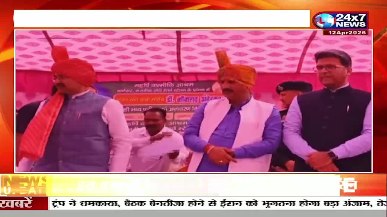 Three men stand on a stage, two wearing vibrant turbans. A banner behind them displays Hindi text, and a JK 24x7 News chyron runs across the bottom of the screen.