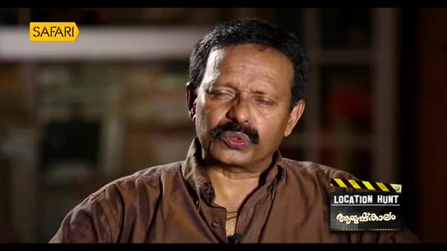A man with a mustache speaks with his eyes closed, his head tilted back slightly. A graphic overlay for "Safari TV" and "Location Hunt" appears on screen.