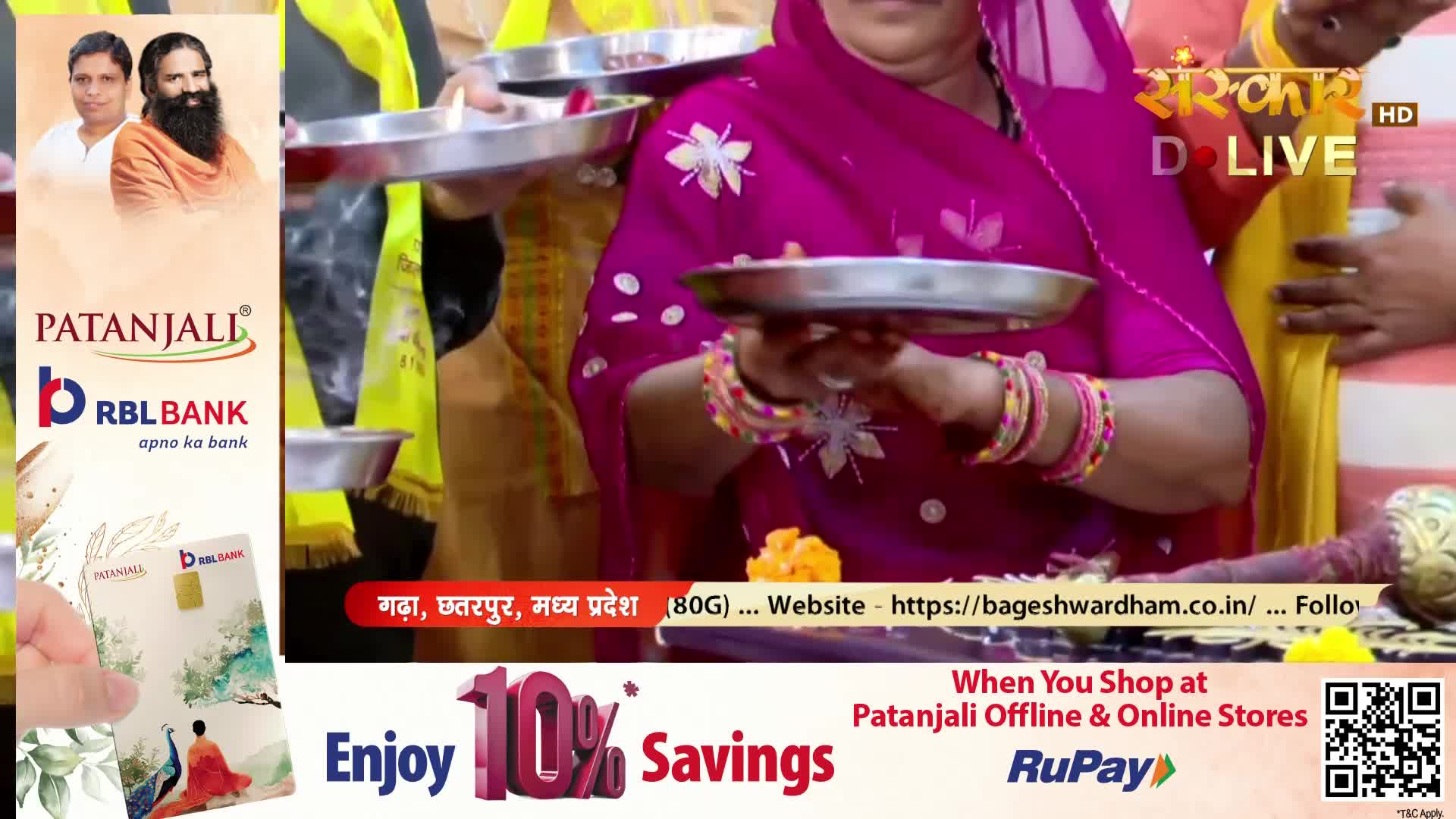 A woman in a bright pink sari holds a silver plate, her bangles jingling. Another person, draped in yellow, offers a similar plate. The Sanskar TV logo is visible in the corner.