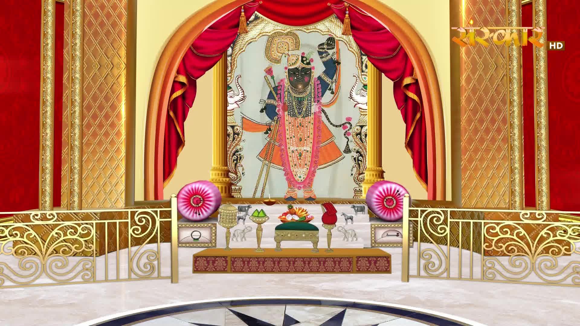 A divine figure stands on a raised platform, adorned in vibrant Indian attire. Red curtains frame the scene, with golden accents and decorative pillows adding to the grandeur.