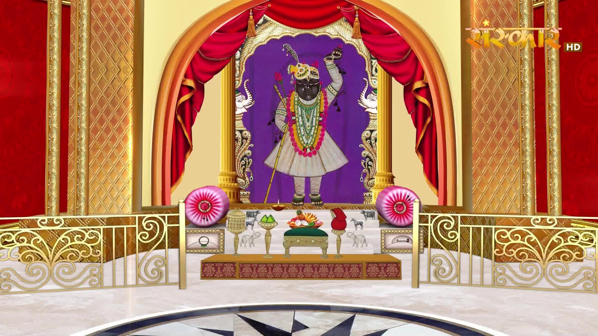A divine figure stands adorned in a white dhoti and vibrant garlands. The Sanskar TV broadcast is set against a backdrop of rich red curtains and ornate gold detailing.