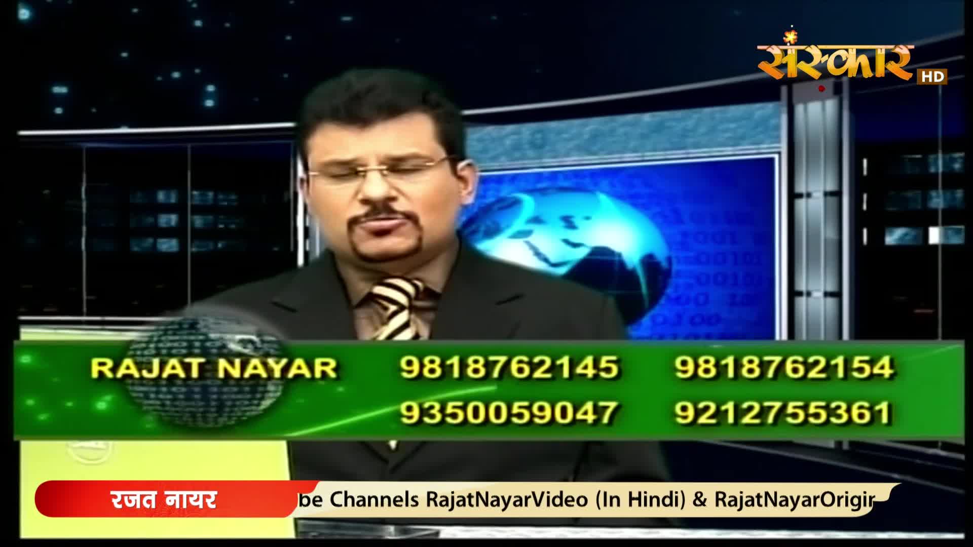 A man in a suit and tie speaks directly to the camera, with a graphic displaying contact numbers and the Sanskar HD logo behind him. The screen behind him shows a blue globe with binary code.