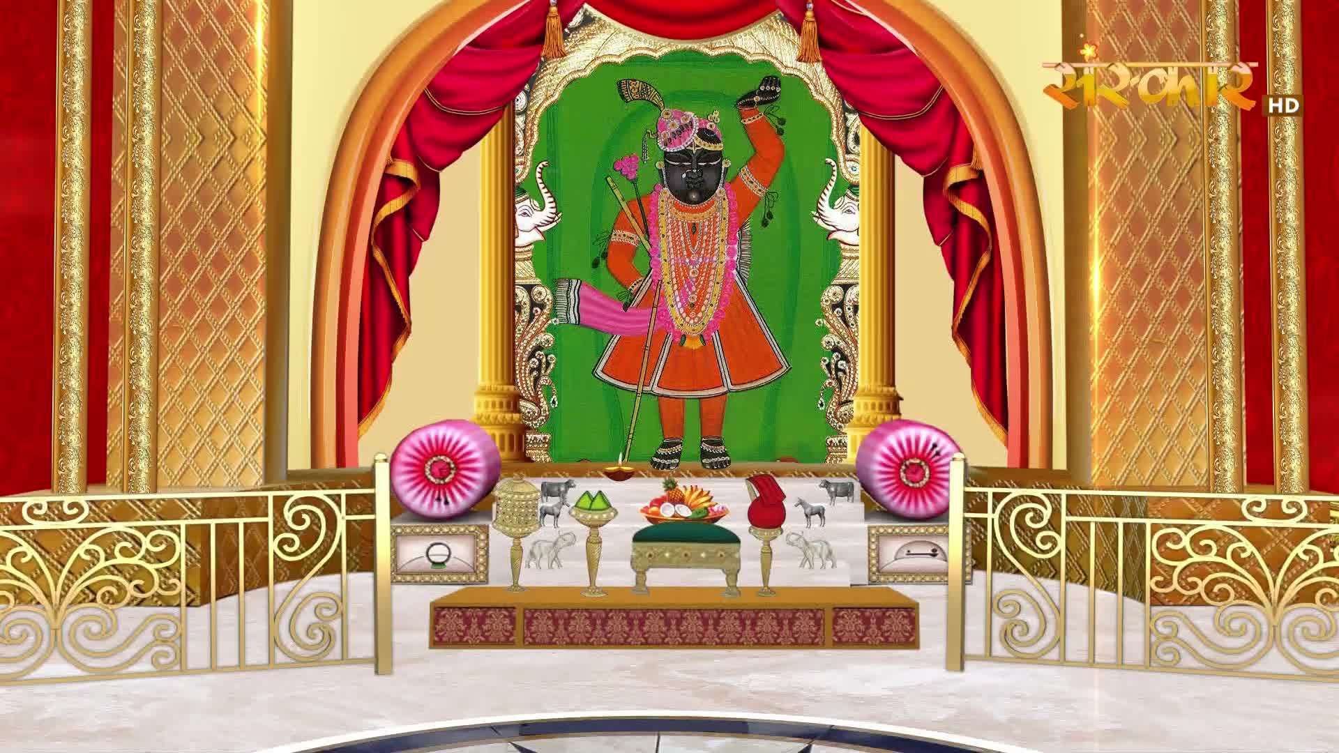 A figure stands adorned in vibrant orange and pink, holding a staff. The scene is set on a stage with ornate gold railings and rich red curtains, reminiscent of a broadcast on Sanskar TV.