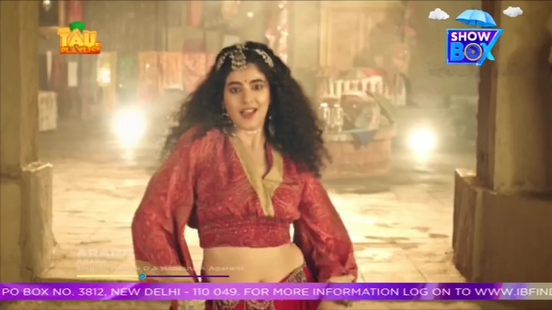 A woman in a red outfit is dancing, her expression animated, in front of what looks like an old building. The ShowBox logo is in the corner, and the scene appears to be from India.
