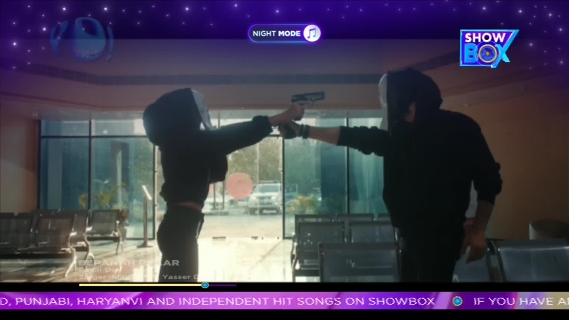 Two figures, both hooded and dressed in black, point handguns at each other. The scene unfolds on a screen, likely a ShowBox video from India, with a "Night Mode" indicator visible.

