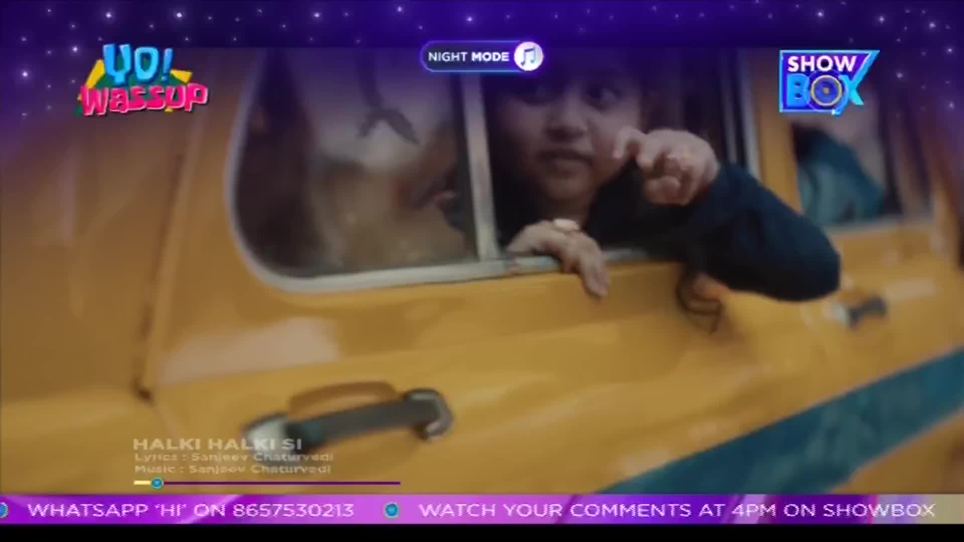 A woman leans out of a yellow vehicle, pointing with one hand. The ShowBox logo is visible, and a song title is displayed on the screen.
