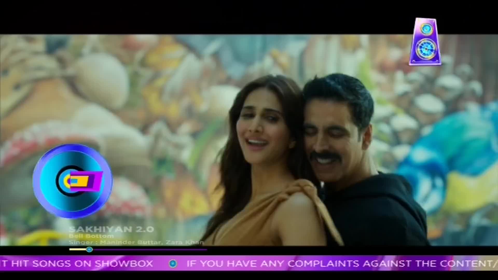 A man with a mustache embraces a woman, both smiling as they face the camera. The scene appears to be a music video, with graphics and text about a song on ShowBox overlaid on the image.
