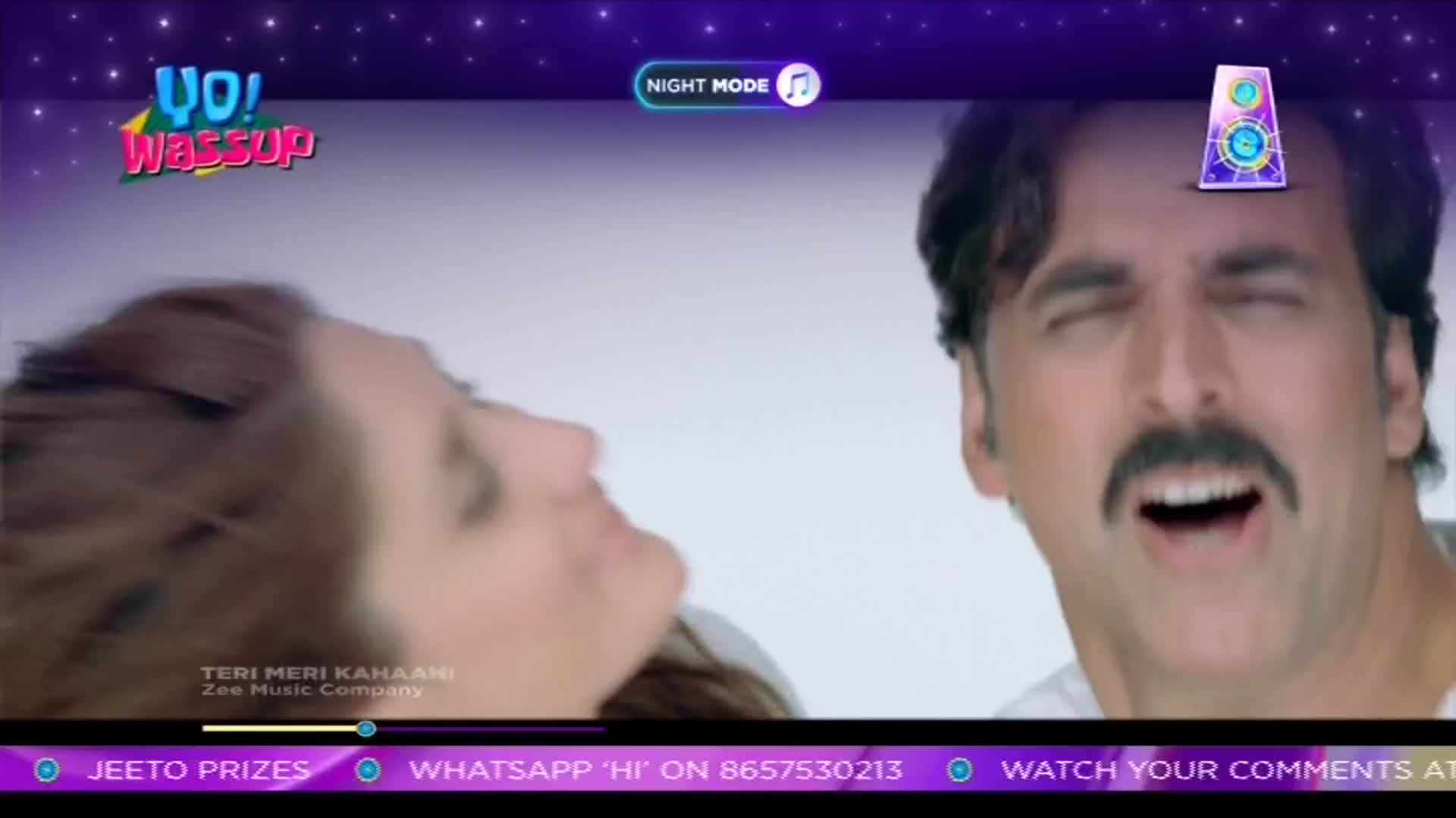 A man with a thick mustache has his mouth wide open, eyes squeezed shut, while a woman's profile is partially visible beside him. The "Yo! Wassup" logo and a "Night Mode" button are at the top of the screen, with a prize-related banner below.
