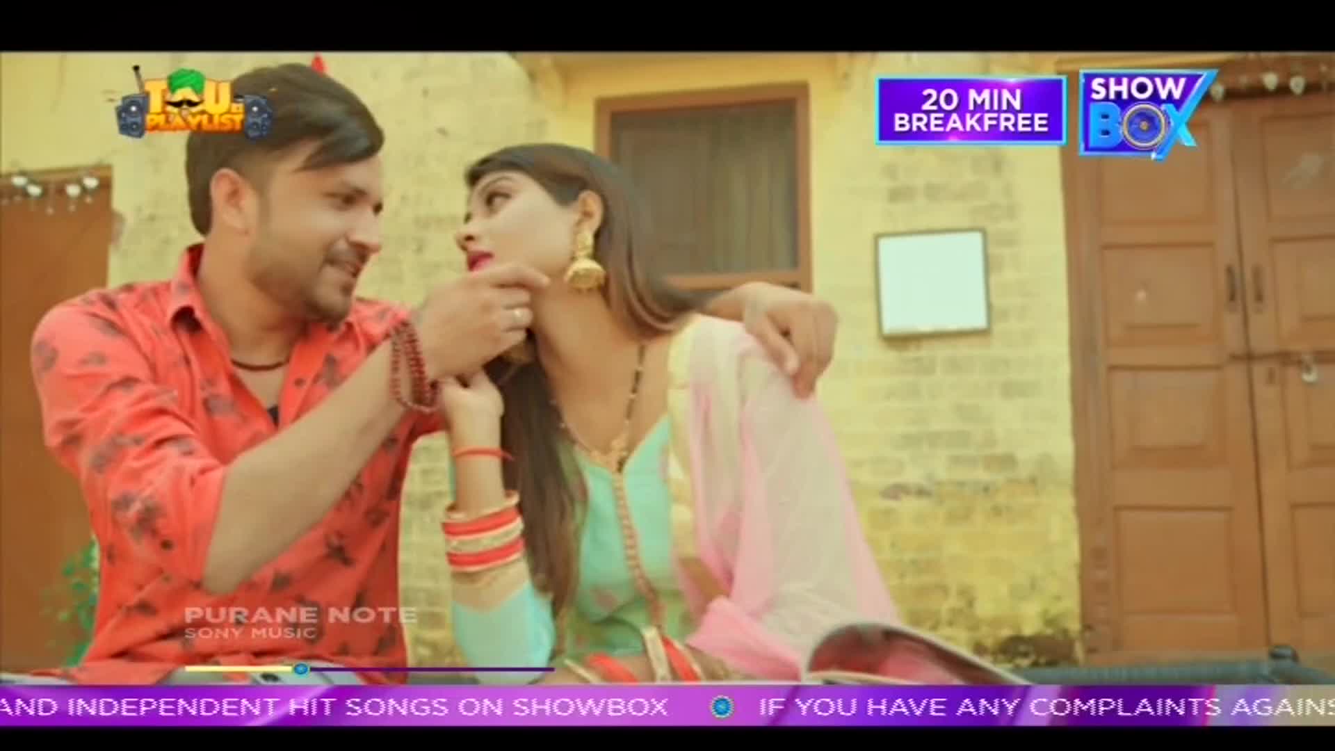A man in a red shirt gently touches a woman's chin as she looks away. They are sitting close together, with a backdrop of a rustic Indian building. A man in a red shirt gently touches a woman's chin as she looks away. They are sitting close together, with a backdrop of a rustic Indian building.
