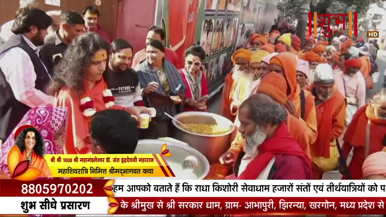 A crowd of men in saffron robes waits patiently as food is ladled from a large pot. A man with long, dark hair, wearing an orange outfit, serves from the pot to a person holding a small cup.